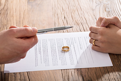 Close-up Of Couple Singing Divorce Agreement With Gold Wedding Ring On Paper
